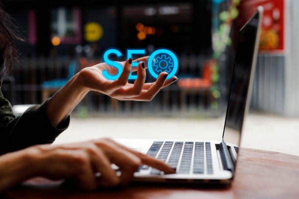 Ecommerce seo services; a hand holding the word SEO in front of a laptop.